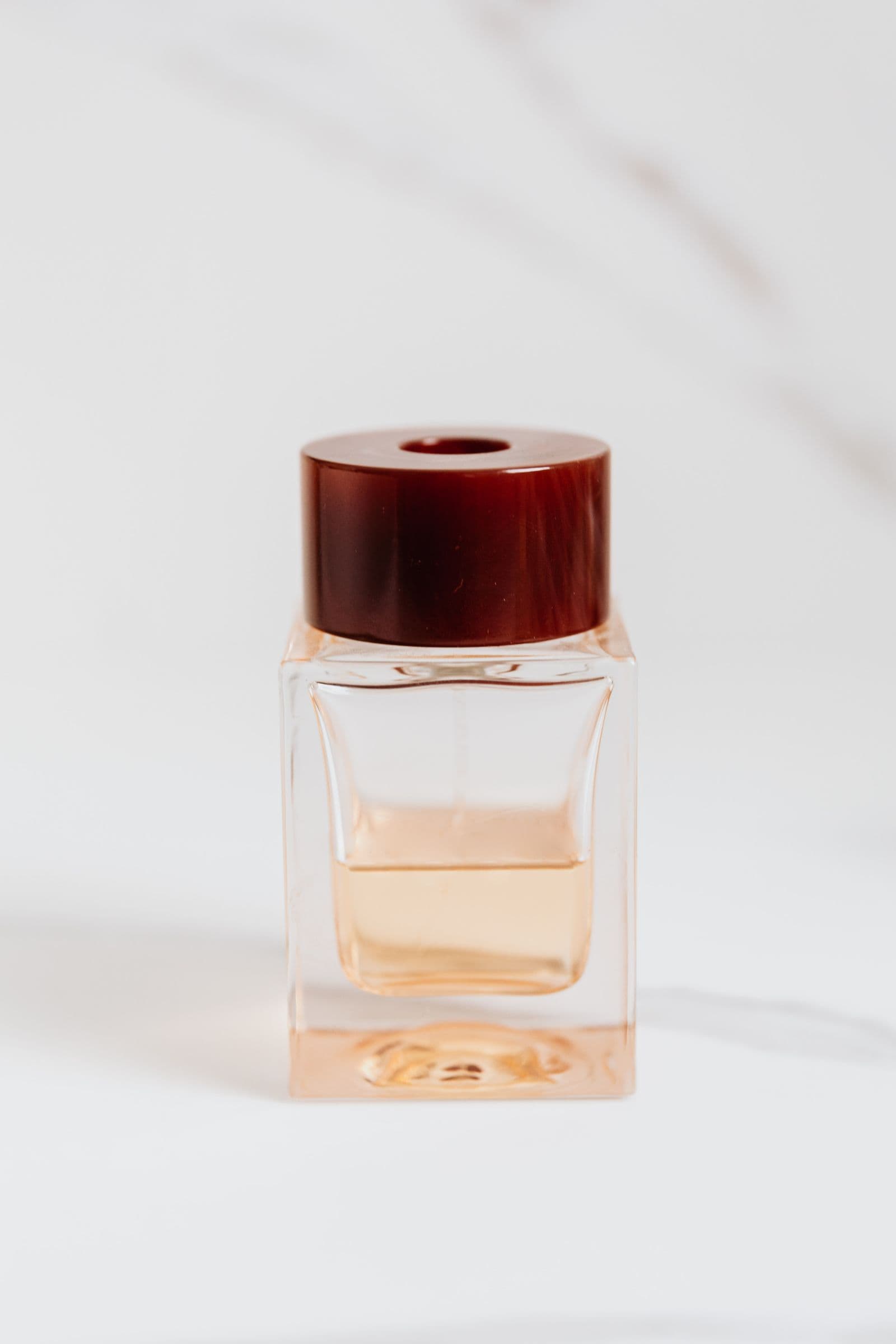Amber Sovereign — a square glass perfume bottle with a burgundy cap and honey-toned liquid, photographed against a softly marbled backdrop