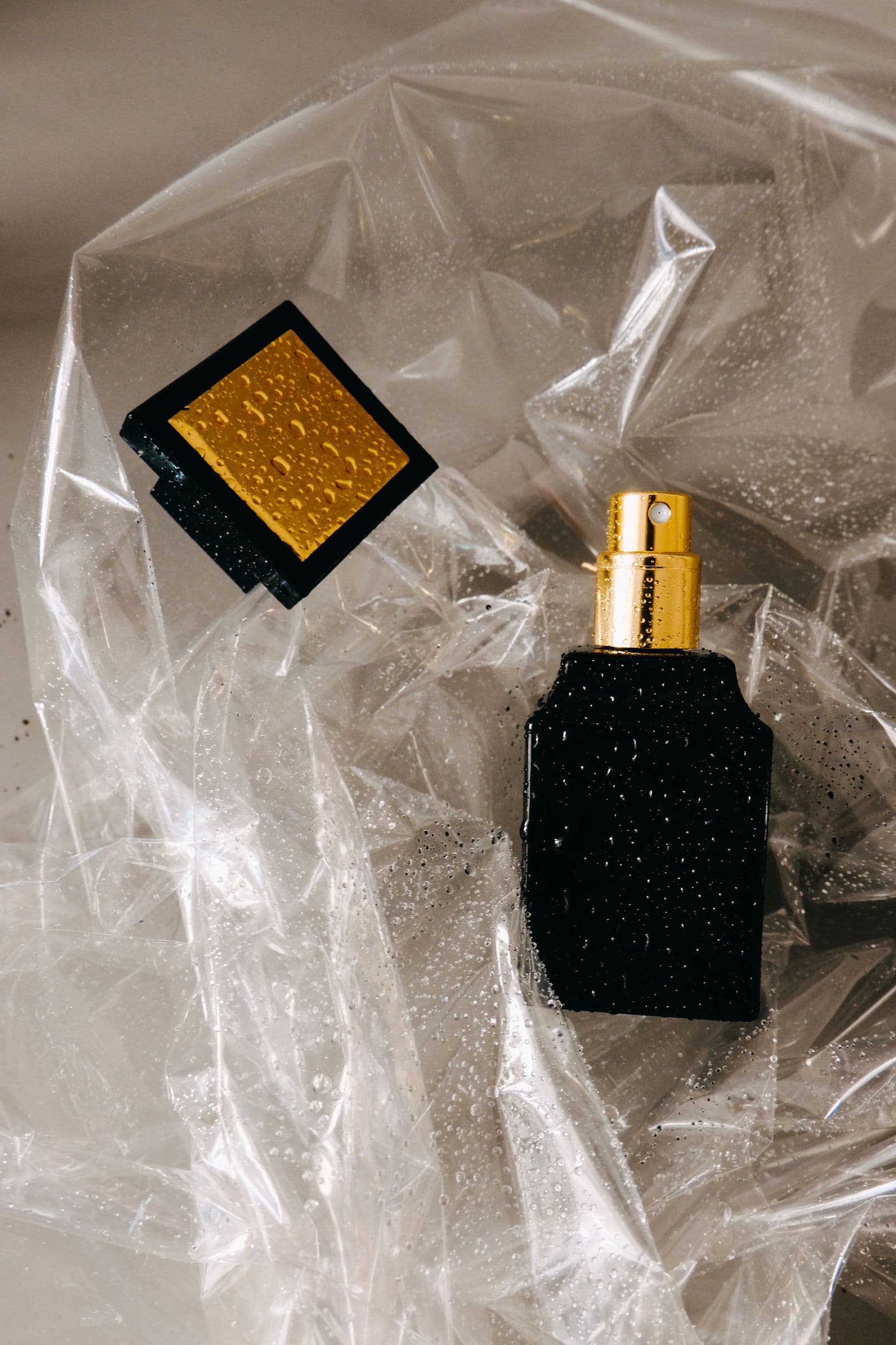 Fauve Noir — a black glass perfume bottle with a gold-trimmed cap, photographed against dark plastic sheeting with soft water droplets